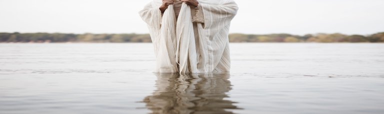 person wearing biblical robe standing water with blurred
